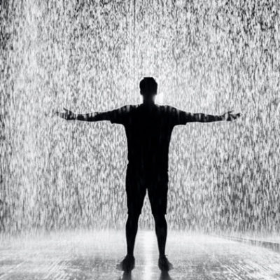 man standing with arms out in rain room