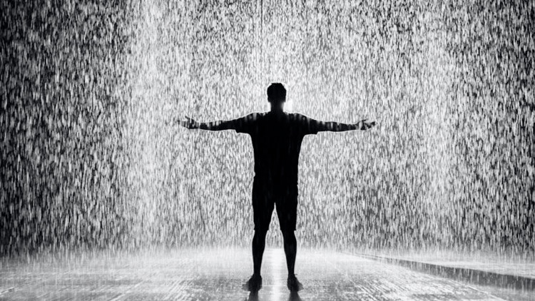 man standing with arms out in rain room