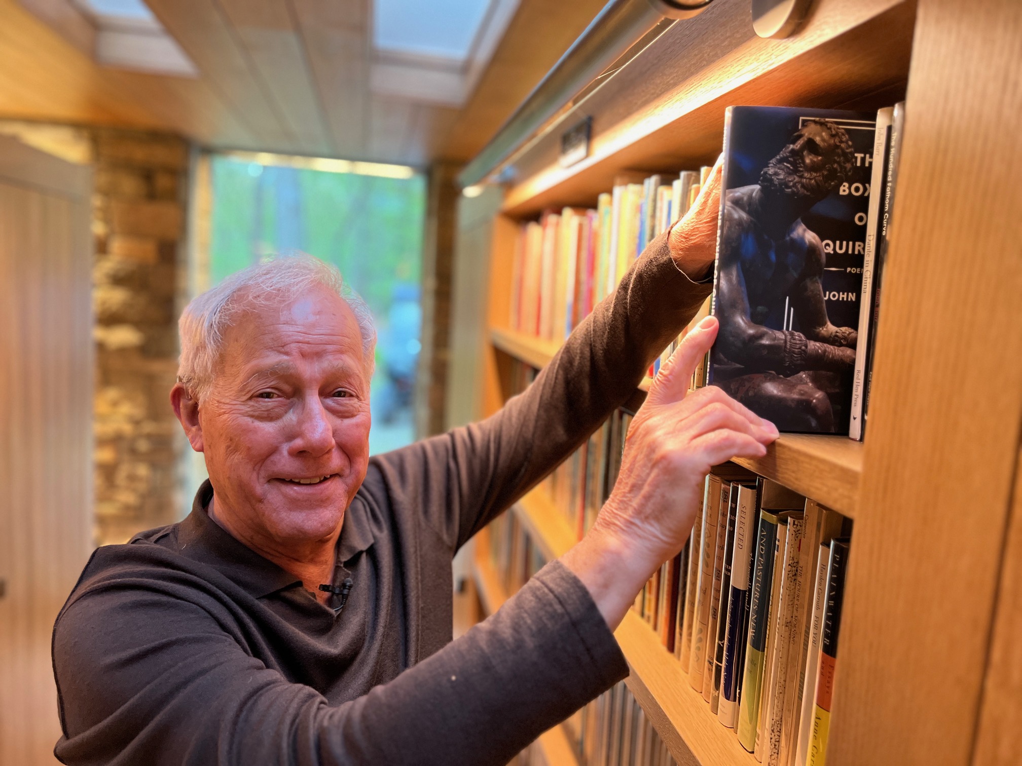 Photo of a man, John Barr, pulling his book of poetry, The Boxer of Quirinal, off a bookshelf